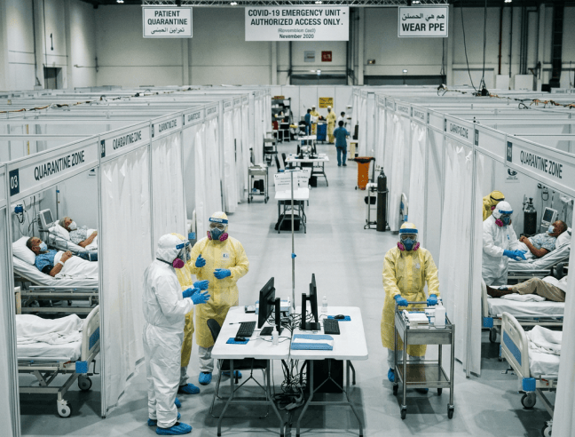 COVID-19 emergency unit with quarantined patients, PPE-clad healthcare workers, and signs reading Wear PPE.